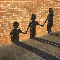 two people holding hands in front of a brick wall with the shadow of a child and an adult