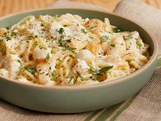 a green bowl filled with pasta covered in parmesan cheese and garnished with herbs