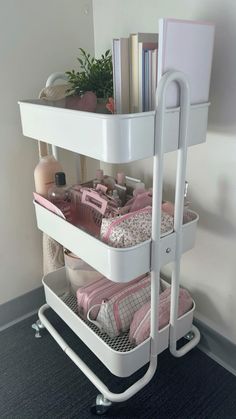 a white shelf with three baskets on top of it and books in the bottom drawer