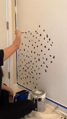 a woman sitting on the floor painting a wall with black dots and paint rollers