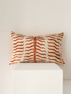 an orange and white pillow sitting on top of a white cube next to a white wall