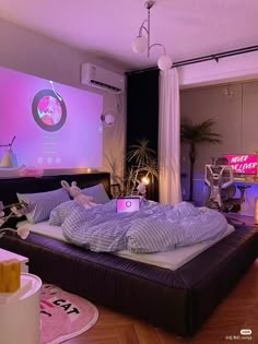 a bed that is in the middle of a room with purple lights on it and a projector screen behind it