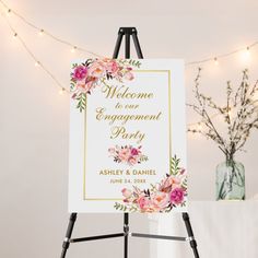 an easel with a welcome sign on it next to a vase and string lights