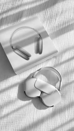 two white headphones sitting on top of a bed next to an object that looks like a pair of earbuds