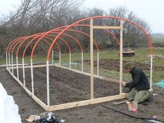 a man is working on an outdoor garden with lots of wood and metal pipes in the ground