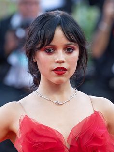 a close up of a person wearing a red dress and posing for the camera with people in the background