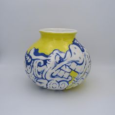 a yellow and blue vase with an intricate design on the front, sitting on a white surface