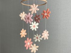 a mobile made out of felt flowers hanging from a wooden rod on a gray wall