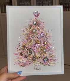 a hand holding up a card with a pink christmas tree in the center and other decorations on it