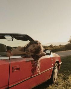 a woman laying down in the back of a red car