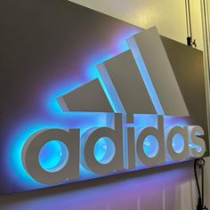 the adidas logo is lit up in blue and purple lights on a gray wall