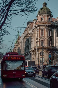 a red bus driving down a street next to tall buildings and traffic lights on a city street