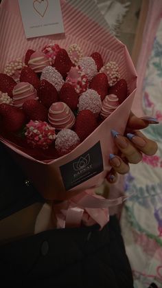 a woman holding a pink box filled with chocolate covered strawberries on top of a bed