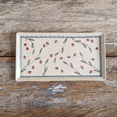 a white plate with red flowers on it sitting on a wooden table next to a piece of wood