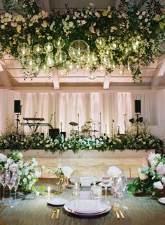 a table set up for an event with flowers and greenery hanging from the ceiling