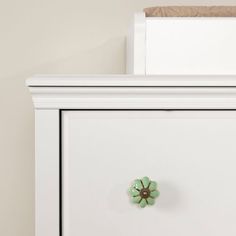 a white dresser with a green flower knob on it