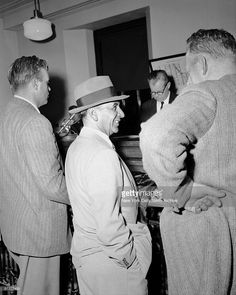 three men in suits and hats are talking to each other while standing near a piano