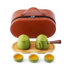 an orange case with four green teas and three cups on a wooden tray next to it