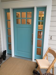 two cats sitting on the front steps of a house next to a blue door and chair