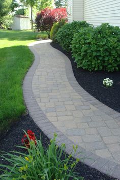 a brick walkway in front of a house with flowers on the side and green grass around it