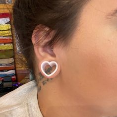 a woman with tattoos on her left ear and behind her ear is a pair of heart shaped earrings