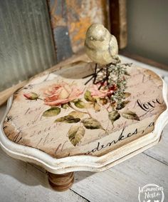 a bird sitting on top of a wooden table with flowers and words painted on it