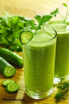 two glasses filled with green smoothie next to cucumbers