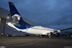 an airplane is parked in front of a hangar at night with people standing around it