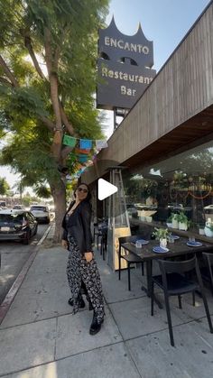 a woman is standing on the sidewalk in front of a restaurant with tables and chairs