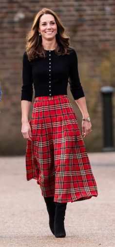 a woman in a red plaid skirt and black cardigan smiles as she walks down the street