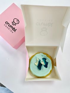 a cupcake with blue icing sitting in a pink box next to a paper bag