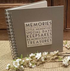 a book with words written on it sitting next to some white flowers and branches in front of a wooden wall