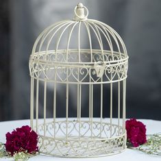 a white birdcage sitting on top of a table next to red carnations