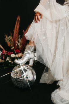 a woman in white dress and high heeled shoes sitting next to a disco ball