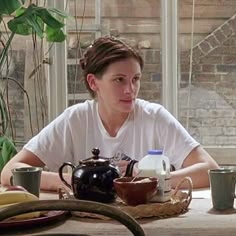 a woman sitting at a table in front of a tea pot and coffee mugs