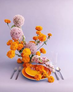 an arrangement of flowers on a table with plates and utensils next to it