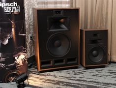 two speakers sitting on top of a carpeted floor next to a wall mounted speaker