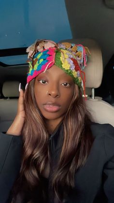 a woman sitting in the back seat of a car wearing a multicolored hat