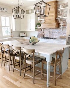 a kitchen with white cabinets and an island in the center, surrounded by wooden chairs