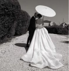 a bride and groom are standing under an umbrella in the middle of a gravel road