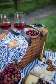 two glasses of wine and cheese on a picnic blanket with grapes, crackers and bread