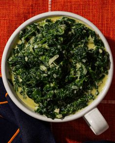 a white bowl filled with spinach and cheese on top of a red table cloth