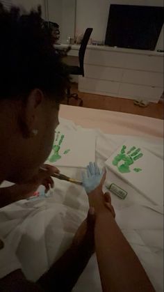 a woman is painting her hands with green handprints on white paper while another person sits in the background