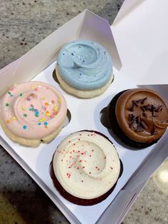 four decorated cupcakes in a box on a table