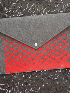 an envelope with red and grey designs on the front is sitting on black fabric, surrounded by sprinkles