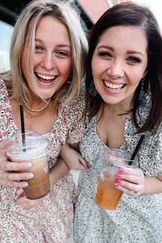 A blonde and brunette woman walking arm in arm through an urban area holding coffee and colorful beverages. They are looking at each other smiling. Both are wearing a ditsy floral mini dress, the blonde in pink and the brunette in blue. The dresses feature a triple ruffle at the shoulder, scoop neckline, smocking at the waist, and a tiered skirt. Floral Spring Dresses, Ditsy Floral Dress, Pink Shades, Blue Or Pink, Body Conscious, Talk Of The Town, Spring Floral Dress