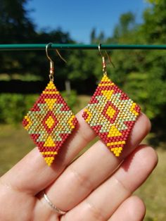 someone is holding up their hand made beaded earrings in front of some trees and bushes