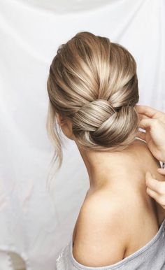 a woman is braiding her hair into a low bun