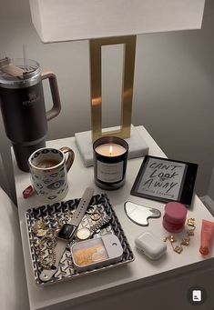 an assortment of personal care items on a table with a coffee cup and lamp in the background