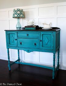 a teal painted buffet table with two white dishes on it and a lamp next to it